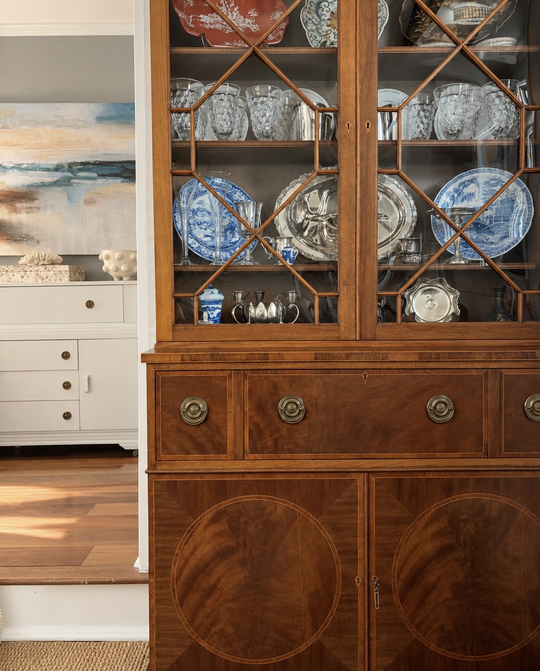 Antique wooden china cabinet displaying blue-and-white porcelain, glassware, and silver