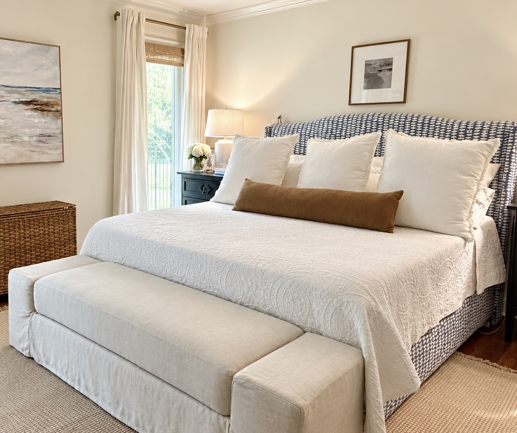 Collected bedroom with a blue patterned upholstered bed, layered white linens, a caramel bolster, and an upholstered bench